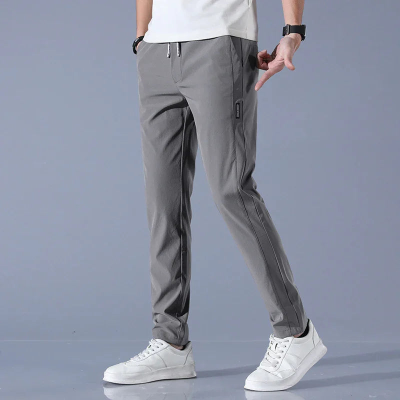 Man wearing casual gray jogger pants with side zipper pocket and white sneakers on gray background