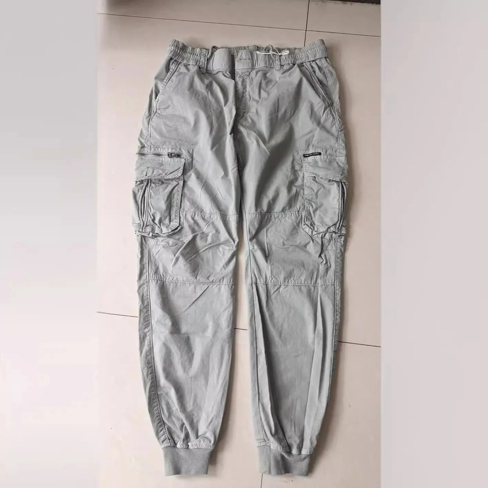 Light gray cargo pants with multiple pockets and elastic cuffs on tiled floor