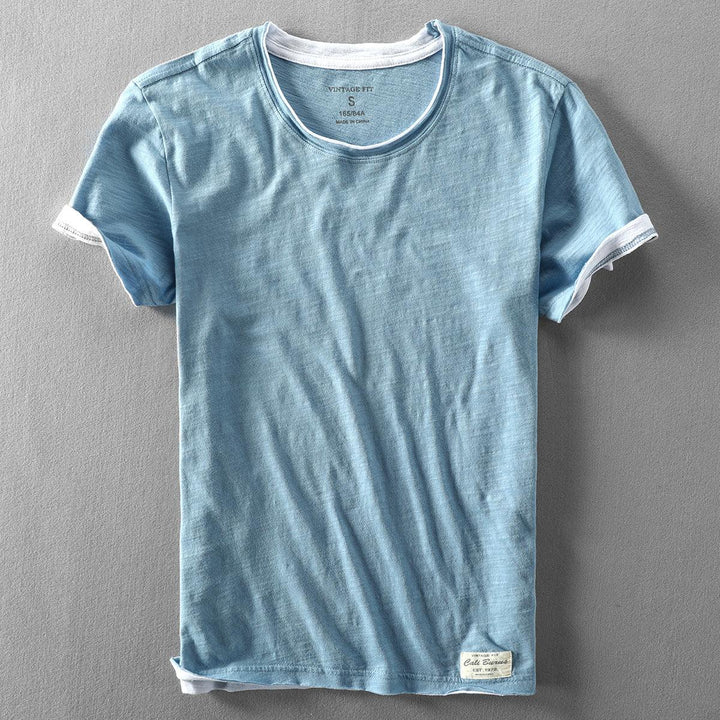 Light blue vintage fit short sleeve t-shirt with white trim on collar and sleeves laid flat on gray surface