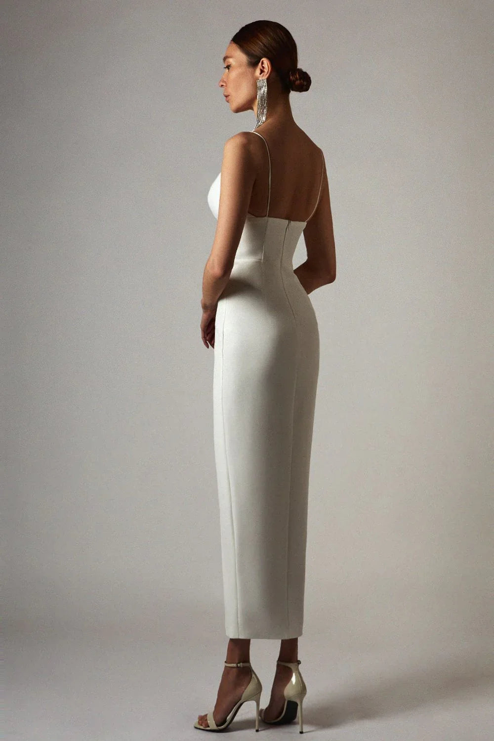 Woman in white form-fitting midi dress with spaghetti straps and high heel sandals in studio