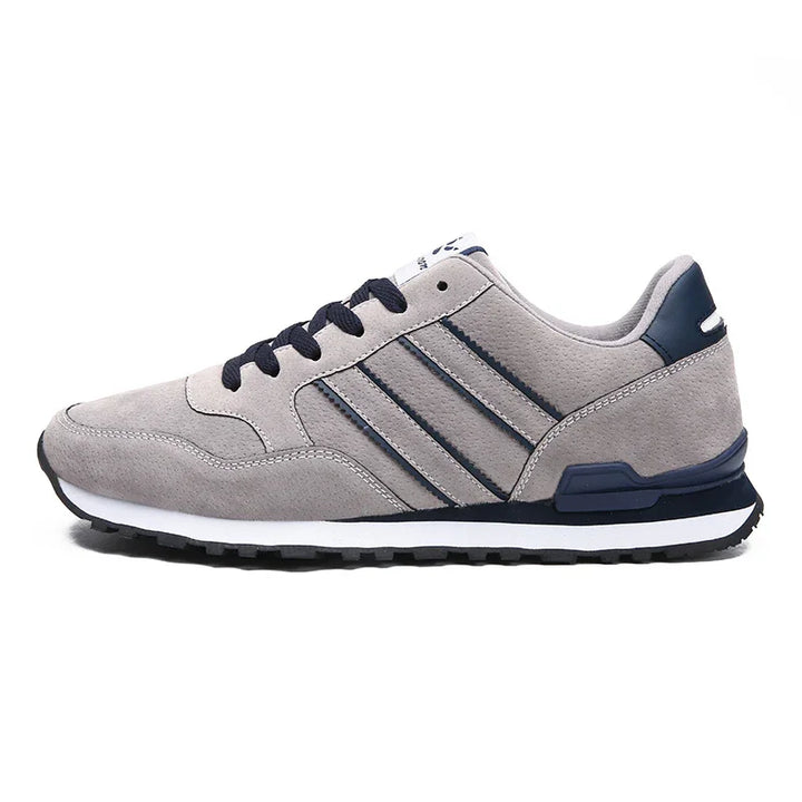 Gray sneaker with navy details, black laces, and white sole on white background