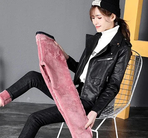 Young woman in black leather jacket and beanie holding pink plush fabric in modern indoor setting
