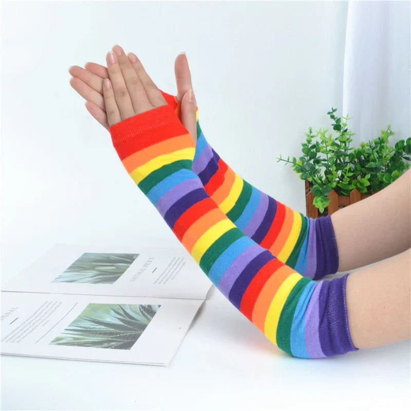 Hands wearing colorful rainbow striped arm warmers over a book with a small green plant in background