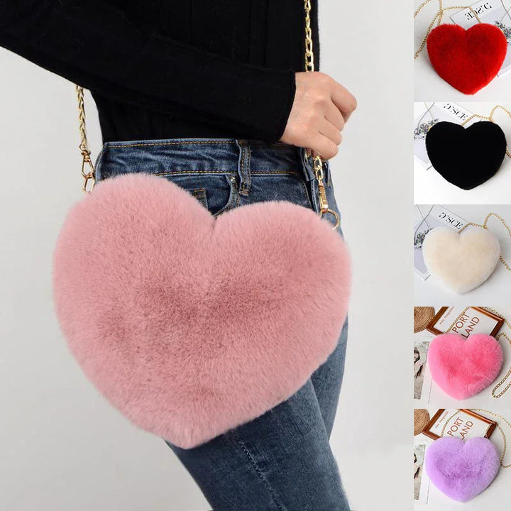 Person wearing fluffy pink heart-shaped crossbody bag with gold chain strap and blue jeans, plus other color options