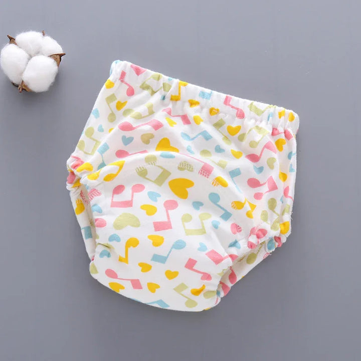 Colorful baby training pants with musical notes and heart patterns on gray background with cotton ball
