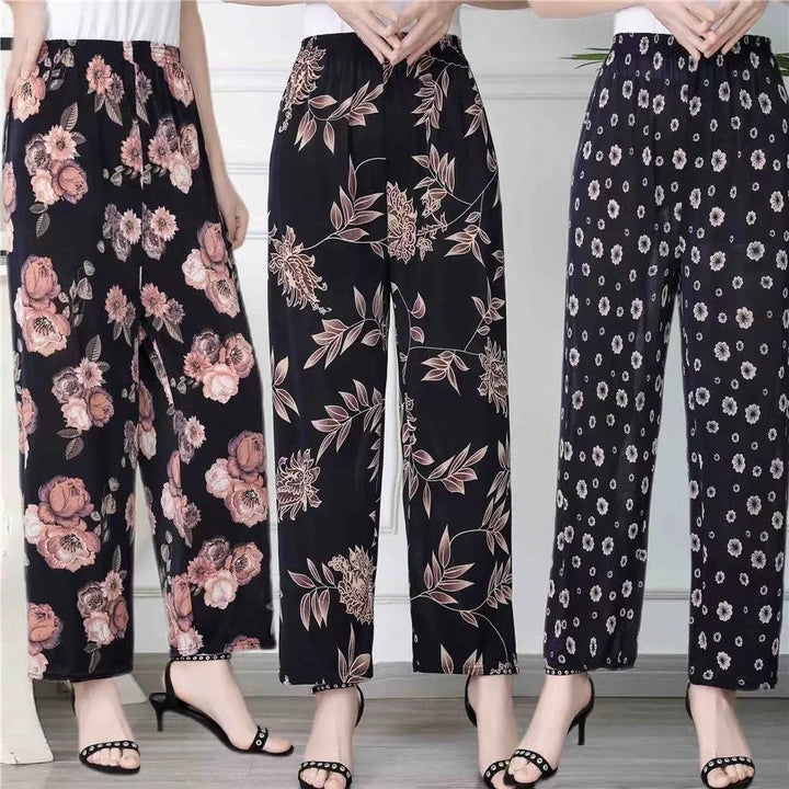 Three women wearing black floral print wide-leg pants with white tops and black heeled sandals