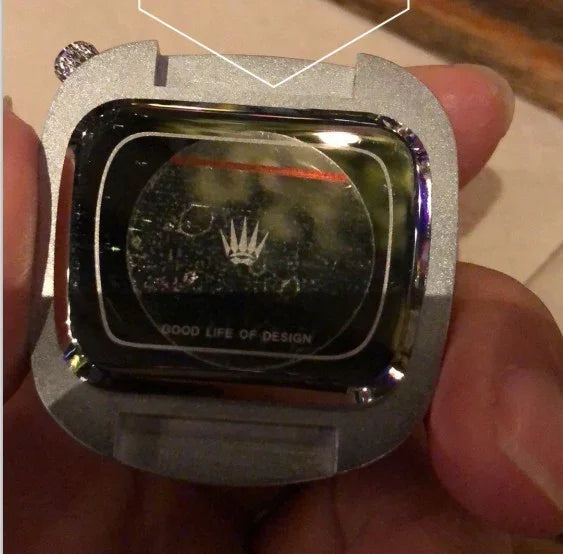 Close-up of a hand holding a silver watch case with a black reflective screen showing a crown logo and the text 'GOOD LIFE OF DESIGN'
