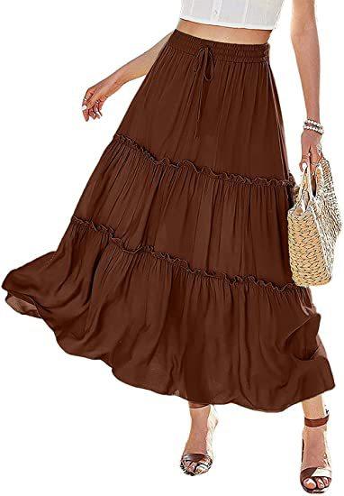 Woman wearing a flowing brown tiered maxi skirt paired with white crop top and sandals, carrying woven bag