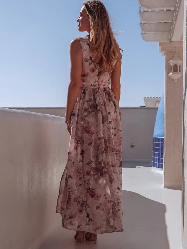 Woman wearing sleeveless floral maxi dress standing on white terrace under clear blue sky