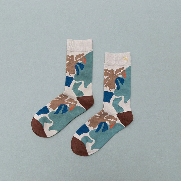 Pair of colorful crew socks with abstract leaf and geometric pattern in blue, brown, beige, and green