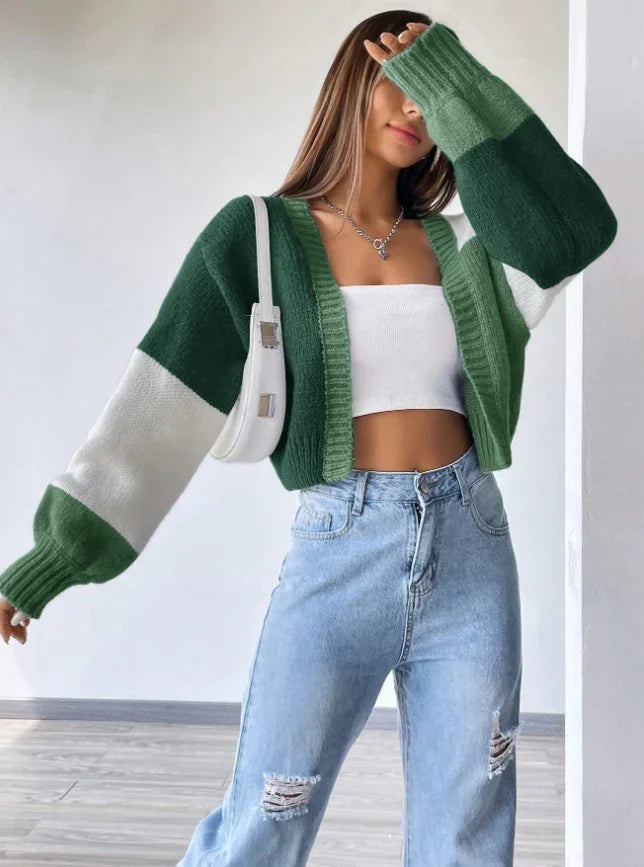 Woman wearing green and white color-block cardigan, white crop top, ripped blue jeans, and white shoulder bag