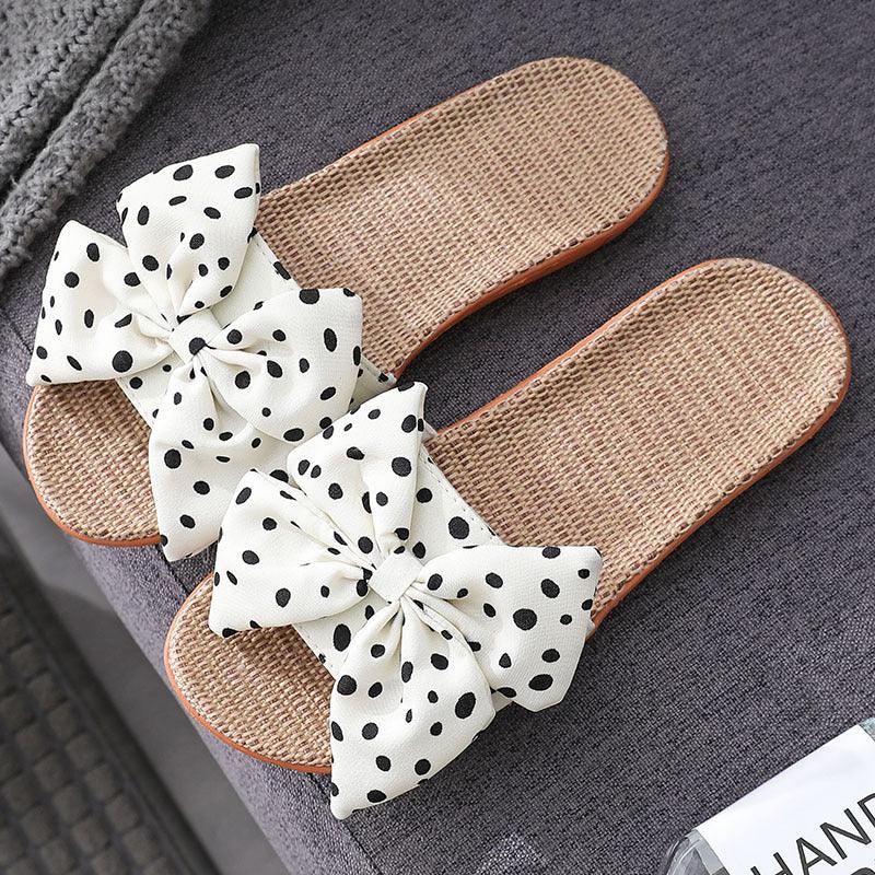 Woven straw sandals with white polka dot bow on grey fabric surface