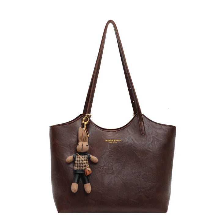 brown leather tote bag with long straps and attached plush bunny keychain
