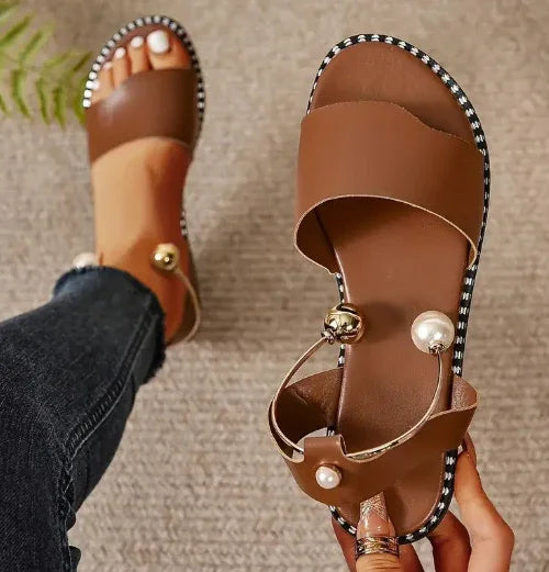 brown leather slide sandals with pearl and gold ball ankle straps on beige carpet