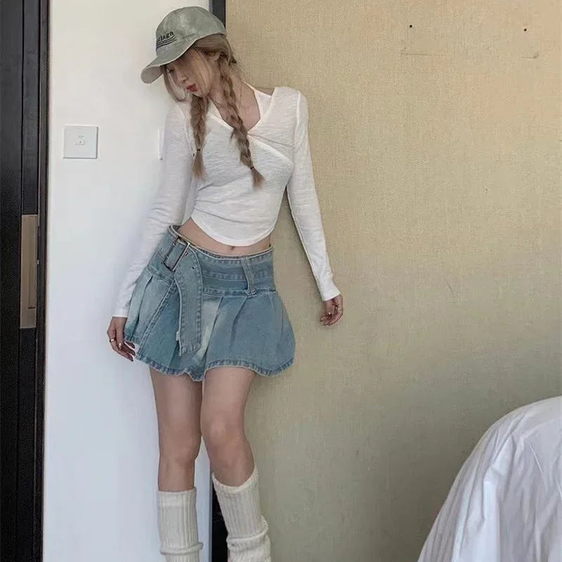 Young woman wearing white long-sleeve top, denim mini skirt, beige cap, and cream knee-high socks indoors