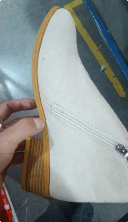 White suede ankle boot with wooden stacked heel and side zipper held by hand indoors