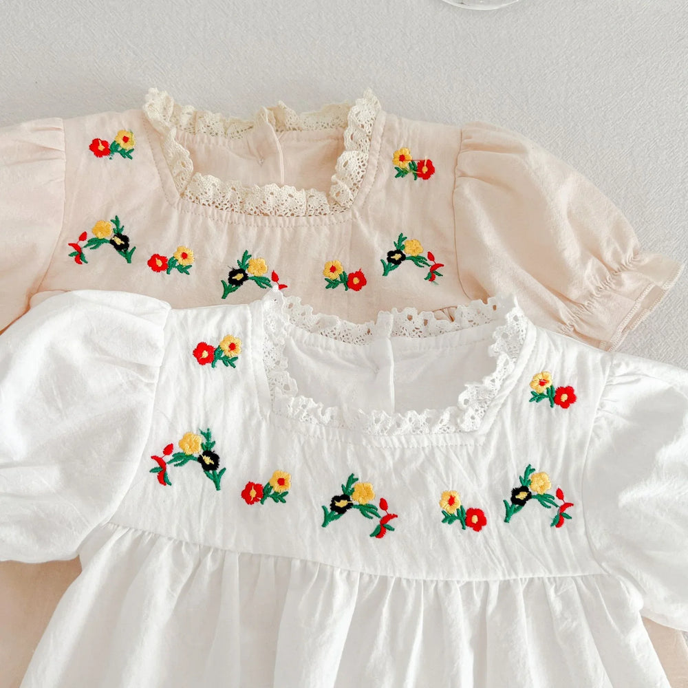 Close-up of baby dresses in white and beige with floral embroidery and lace neckline detail