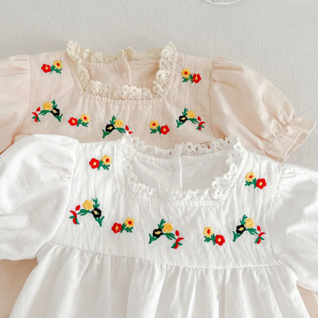 Close-up of baby dresses in white and beige with floral embroidery and lace neckline detail