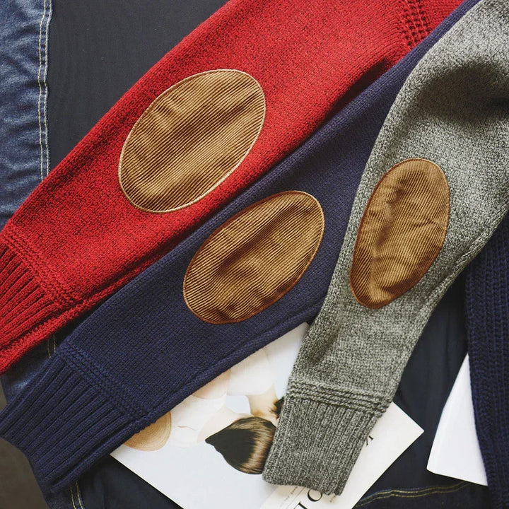 Close-up of red, navy blue, and gray knit sweaters with brown corduroy elbow patches on a dark fabric surface
