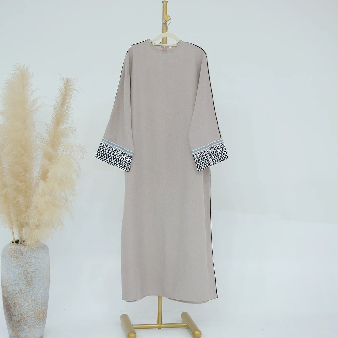 Beige long dress with patterned sleeve cuffs on gold stand next to pampas grass vase