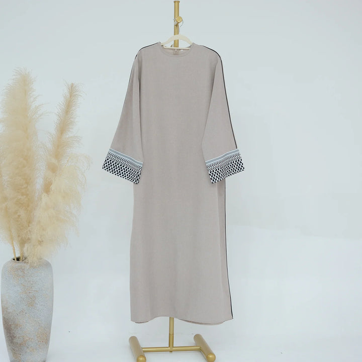 Beige long dress with patterned sleeve cuffs on gold stand next to pampas grass vase
