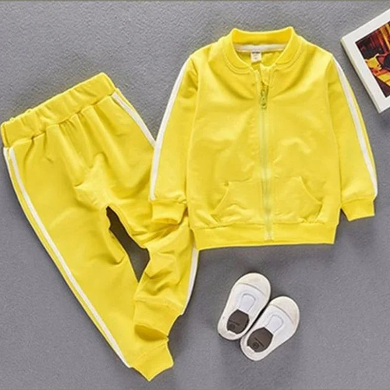 Yellow toddler tracksuit with white stripes, zip-up jacket and elastic pants, paired with white toddler shoes on gray background