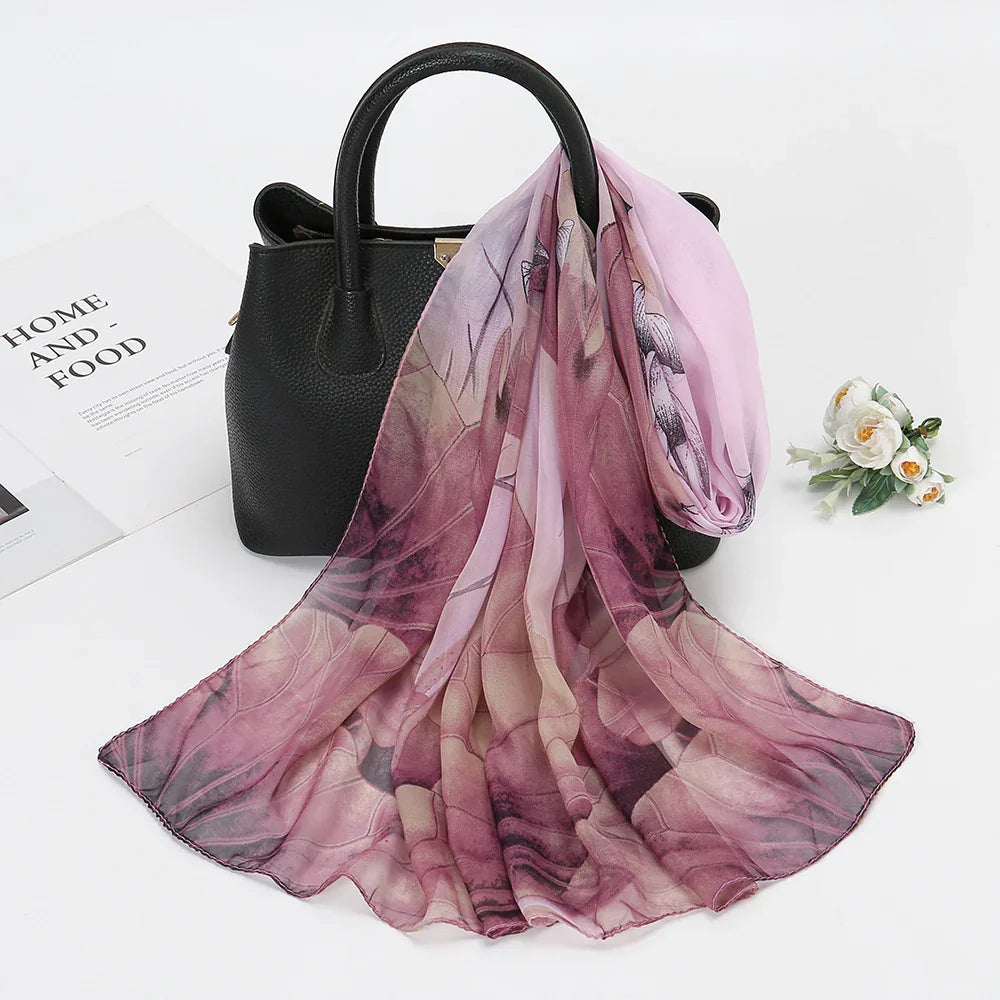 Black leather handbag with a flowing pink floral patterned scarf draped over it on a white surface