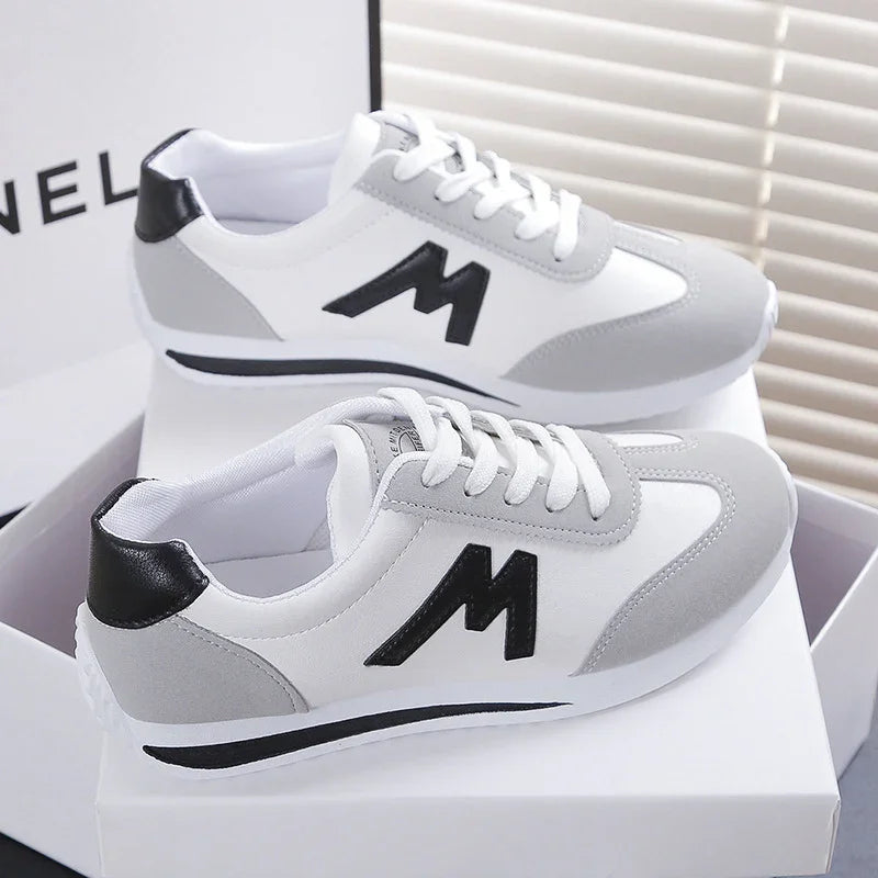 White and gray sneakers with black M logo and laces on white box, stylish casual shoes