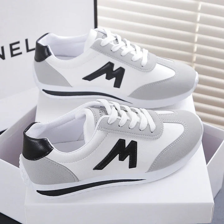 White and gray sneakers with black M logo and laces on white box, stylish casual shoes