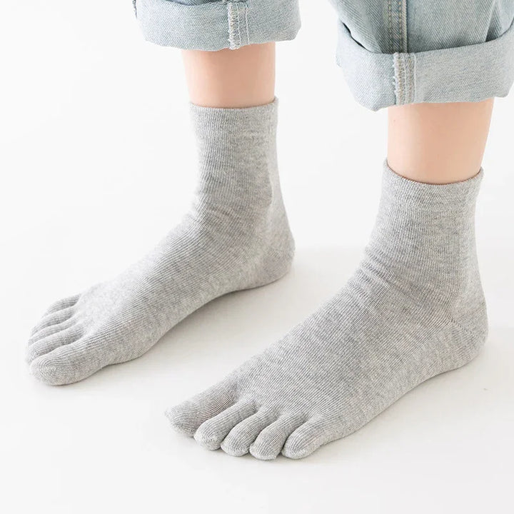 Person wearing light gray toe socks paired with rolled-up light blue jeans on white background