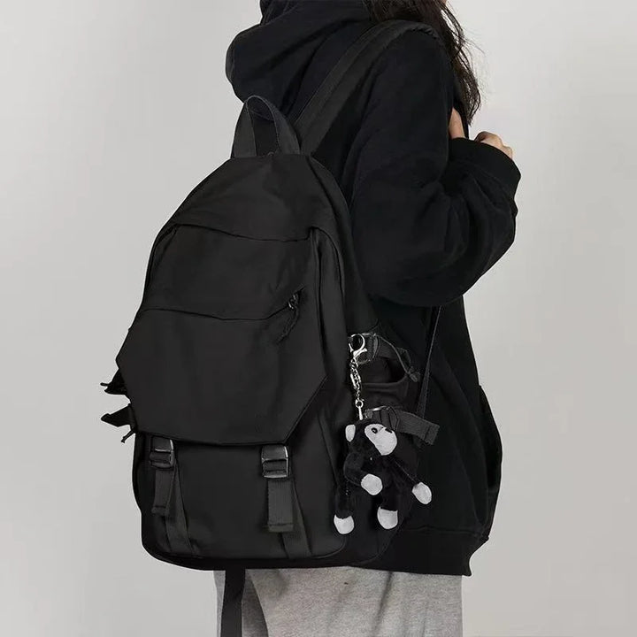 Person wearing black hoodie and gray pants carrying black backpack with small black and white teddy bear keychain