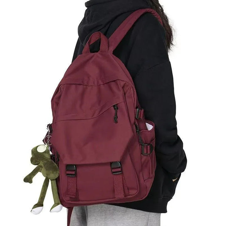 Person wearing maroon backpack with multiple pockets and green plush frog keychain