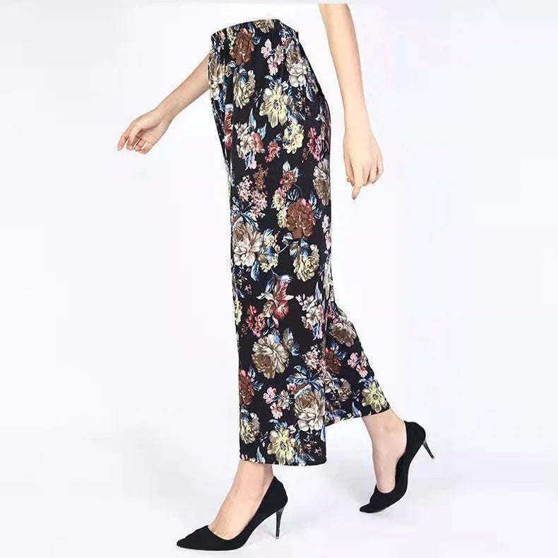 Woman wearing black wide-leg floral pants with elastic waist and black high heels walking