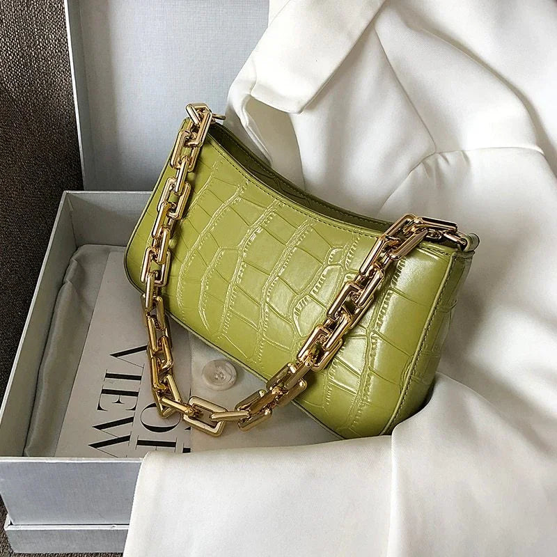 Green crocodile texture handbag with gold chain strap on white fabric inside grey box