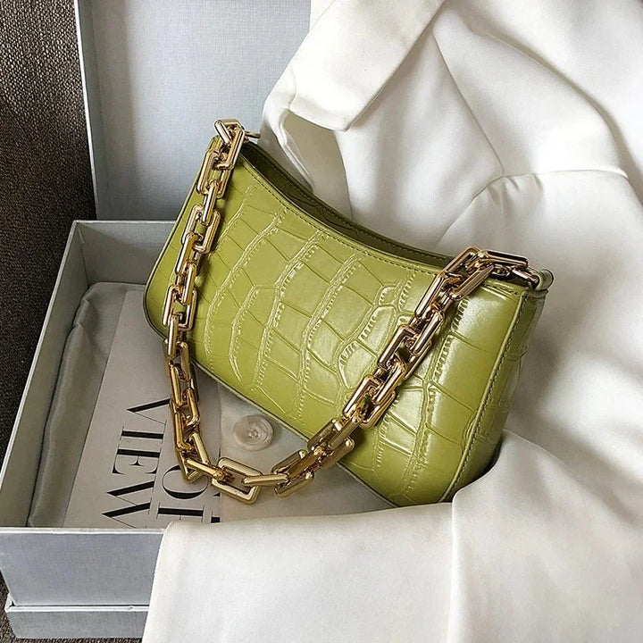 Green crocodile texture handbag with gold chain strap on white fabric inside grey box