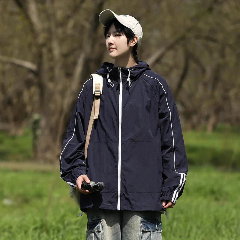 Person wearing navy windbreaker and beige cap holding binoculars in green outdoor setting