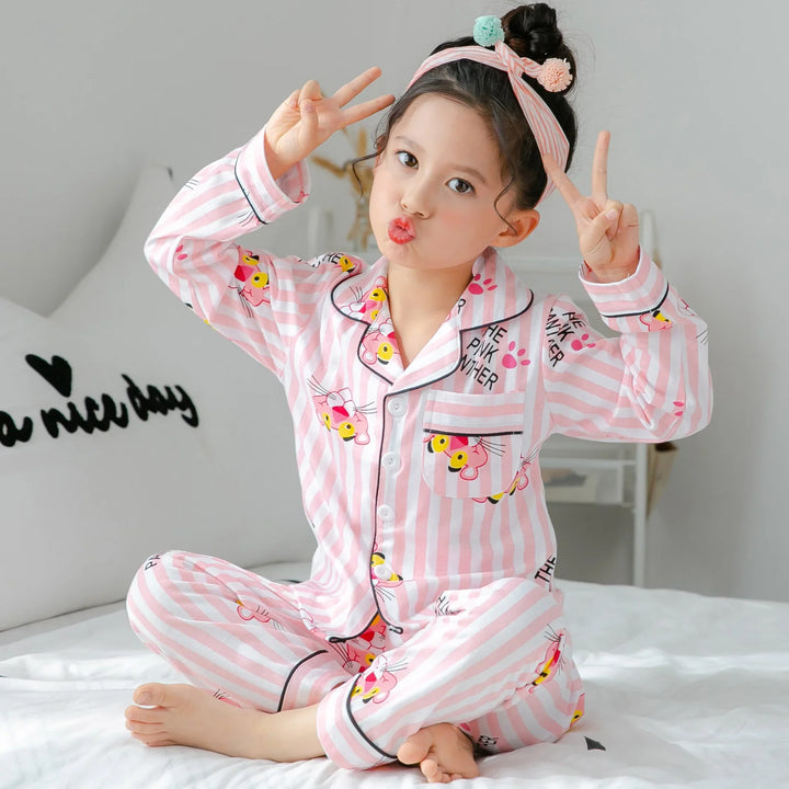 Child in pink striped pajamas with cartoon pink panther, sitting on bed making peace signs