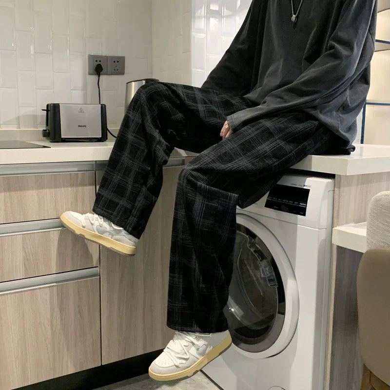 Person wearing black plaid pants and white sneakers sitting on kitchen counter next to washing machine
