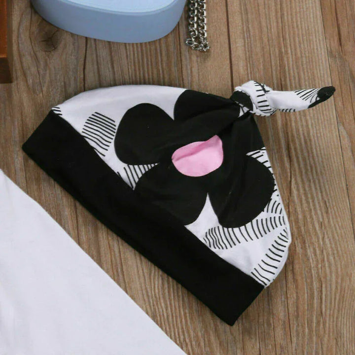 Black and white baby hat with a large black flower and pink center, knotted top, on wooden surface