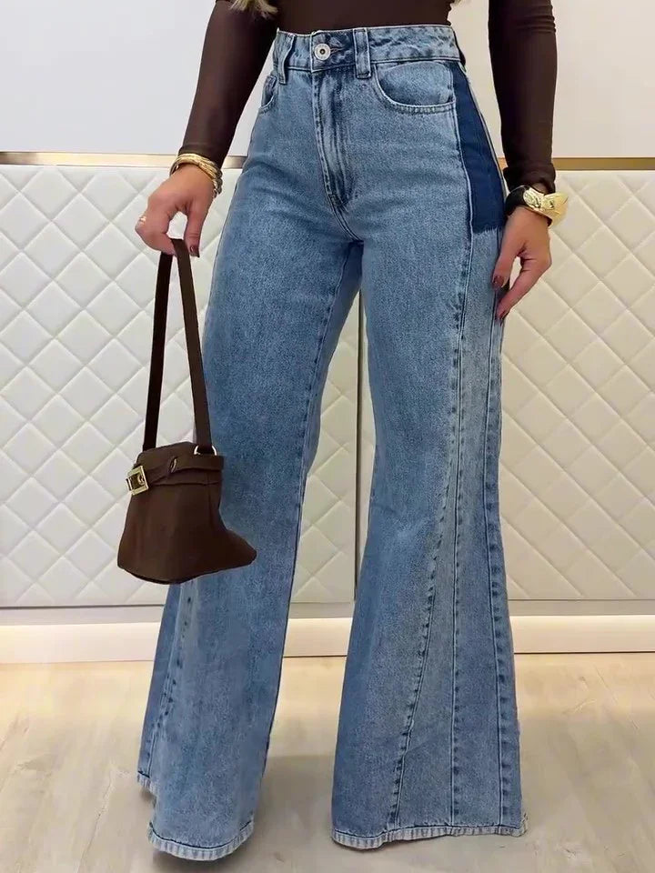 Woman wearing light blue wide-leg jeans with dark side panels holding a small brown handbag
