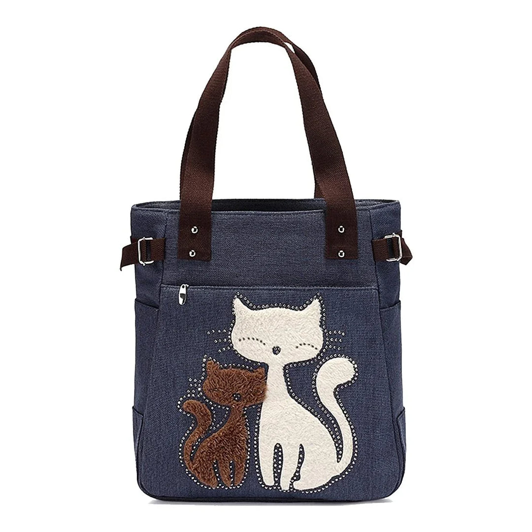 Blue tote bag with brown handles featuring cute white and brown cat embroidery and front zip pocket