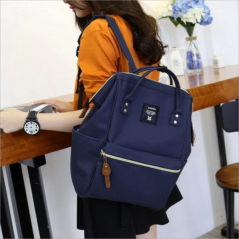 Woman wearing orange top and black skirt carrying navy anello backpack with front zipper pocket indoors