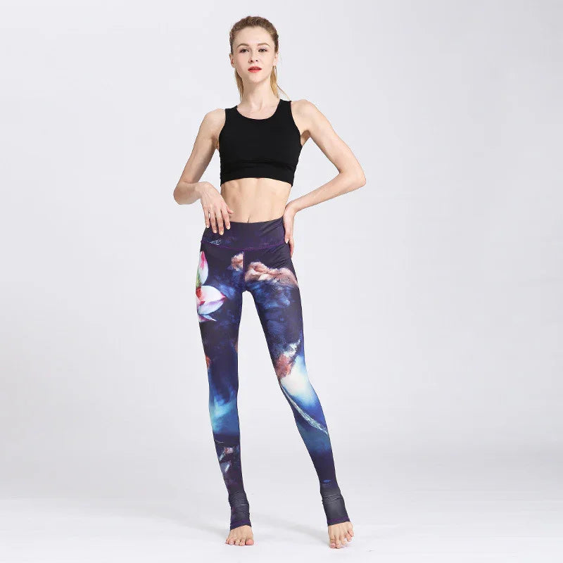 Woman wearing black sports bra and colorful galaxy print leggings posing barefoot on plain background