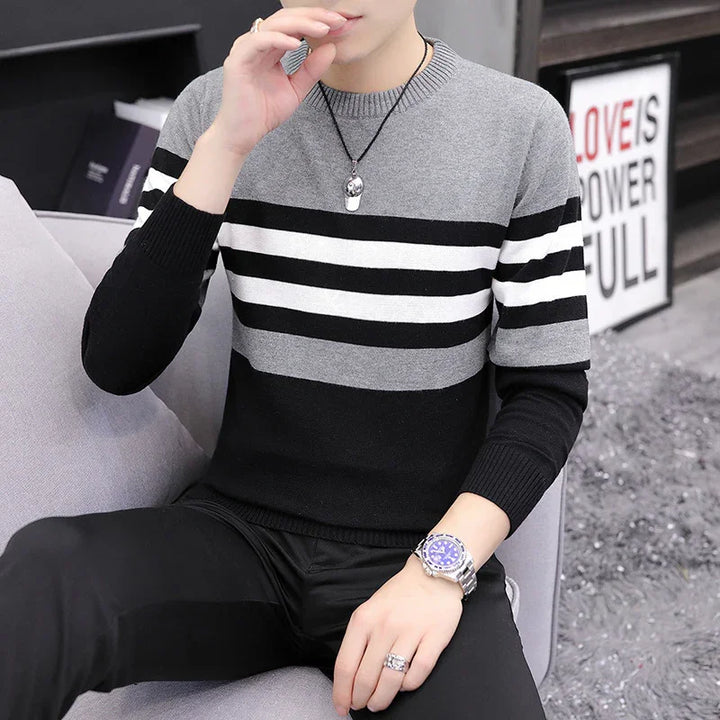 Man wearing black, gray, and white striped sweater with silver watch and skull necklace sitting on gray couch