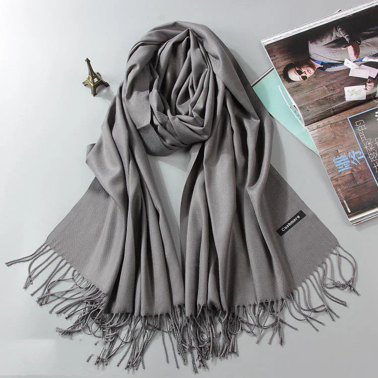 Soft gray cashmere scarf with fringed edges displayed with Eiffel Tower figurine and magazine