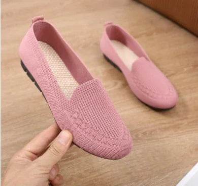 Light pink knitted slip-on flat shoes with textured pattern on wooden floor