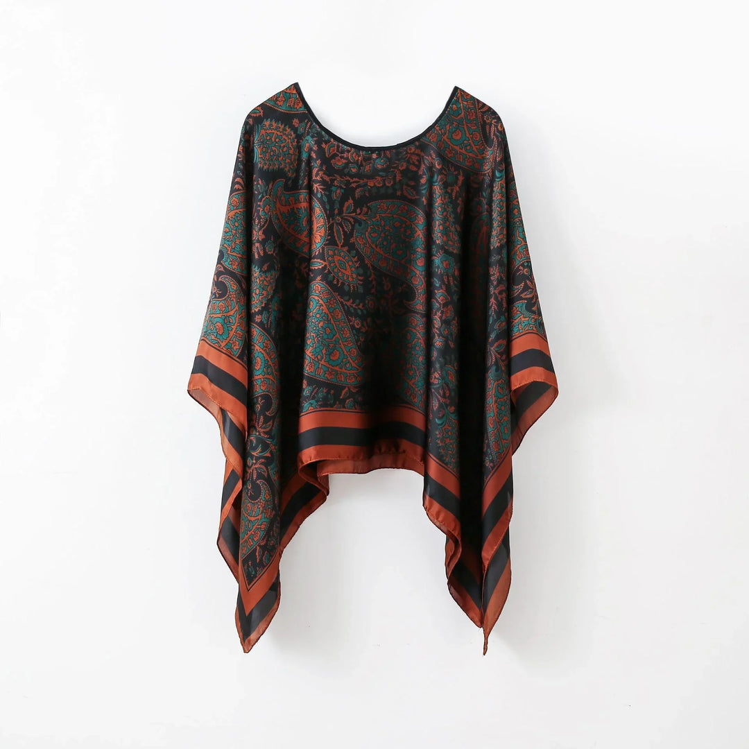 Black and rust patterned poncho with paisley print and striped border hanging on white wall