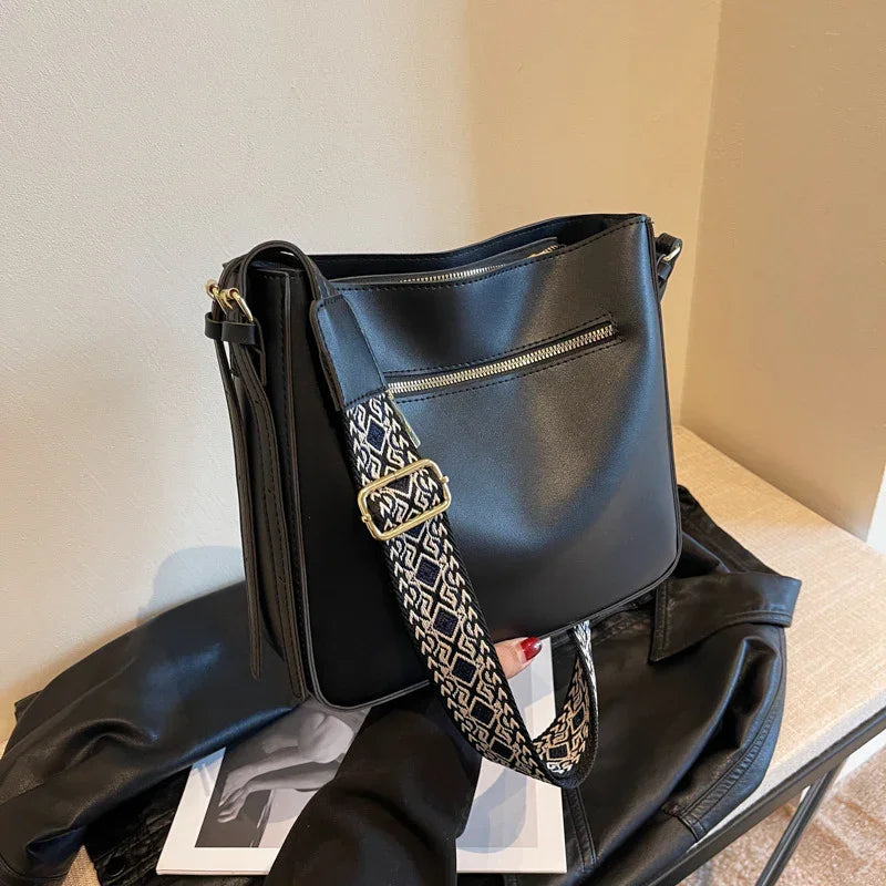 Black leather crossbody bag with patterned adjustable strap and front zipper pocket on leather jacket