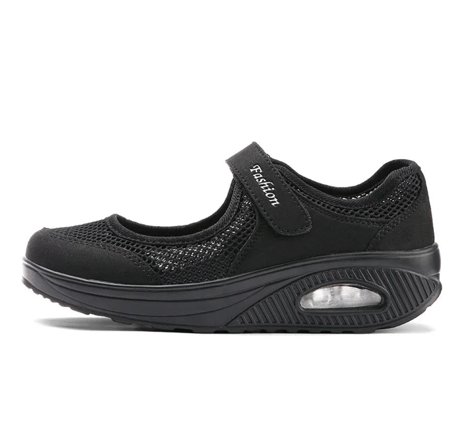 Black mesh Mary Jane flat shoe with cushioned sole and velcro strap labeled Fashion