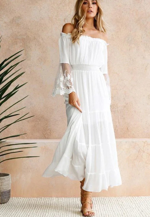 Blonde woman wearing a white off-shoulder bohemian maxi dress with lace bell sleeves and tan sandals